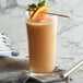A glass of orange liquid with a straw and fruit on top.