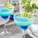 Two blue drinks with lime garnish on a table in a cocktail bar.