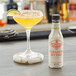 A glass of yellow margarita next to a bottle of Fee Brothers Spicy Habanero Bitters.
