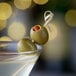 A close up of a green olive in a martini glass.