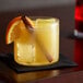 A glass of yellow liquid with an orange slice and a cinnamon stick on a table.