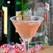 A close-up of a martini glass with a peppermint candy cane rim on a pink drink.