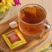 A glass cup of Twinings Earl Grey tea with a bag on a tray next to a flower.