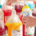 A person pouring Hawaiian Shaved Ice Banana Snow Cone Syrup from a bottle into a cup.