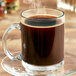 A glass mug filled with brown Ellis Hazelnutty coffee with steam coming out of it.