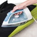 A person's hand using a Hamilton Beach HIR750 full size hospitality iron on a black cloth.