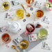 A table with a glass cup of Numi Organic Mate Lemon tea and a tea bag in it, surrounded by tea bags and teapots.