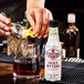 A hand pours Fee Brothers Mole Bitters into a glass of ice on a bar counter.