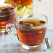 A Numi Organic Breakfast Blend tea bag in a glass cup of brown liquid on a table with a blue plate.