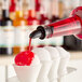 A person pouring Hawaiian Shaved Ice Cherry Snow Cone Syrup into a bowl of snow cones.