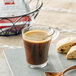 A glass cup of illy espresso with a pastry on a plate.