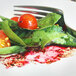 A fork on a plate with a leafy green salad topped with a tomato and pink salt flakes.