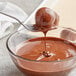 A spoon dipping into a bowl of liquid dark chocolate.