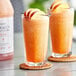 Two glasses of Narvon Peach frozen cocktail with peach slices on a table.