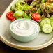 A plate of salad with a bowl of white dressing on it.