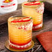 Two glasses of orange and yellow drinks with a red pepper on top.