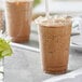 A plastic cup with a straw and brown liquid with a leaf on the rim.