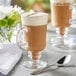 A glass mug of Capora Vanilla Chai Latte with a spoon on the table.