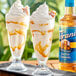 Two glasses of ice cream sundaes topped with Torani Sugar-Free Salted Caramel syrup with a white and brown liquid.