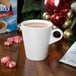 A white mug filled with hot cocoa sits on a wooden surface surrounded by peppermint candies and holiday decorations.