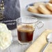 A glass cup of Lavazza espresso on a saucer next to a plate of cookies with a spoon.