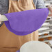 A person rolling out purple Satin Ice chocolate-flavored rolled fondant with a purple rolling pin on a white surface.