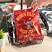 A hand holding a red Bronco Billy's Sweet Heat Beef Jerky packet in a black wire basket on a counter.