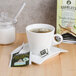 A cup of Bromley Temple of Heaven Green Tea on a saucer with a bag in it on a table next to a box of tea.