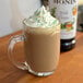 A glass mug of Monin Irish Cream flavoring syrup in coffee with whipped cream on top.