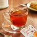 A glass cup of Bigelow pumpkin spice tea with a tea bag on a saucer.