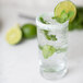 A glass of water with mint and limes on a table with a Rokz Mojito Cocktail rimmed glass.