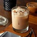 A glass of liquid with ice and a straw sitting on a wooden surface.