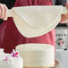 A person using Satin Ice Tropical White Rolled Fondant to decorate a cake with flowers using a rolling pin.