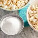 A bowl of popcorn with a bowl of white powder on the side.