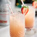 Two glasses of pink Monin Strawberry Rhubarb drinks with straws and a strawberry on top.