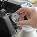 A hand holding a round silver Ellis Philadelphia Roast coffee single serve cup over a coffee machine.