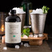 A Woodford Reserve Mint Julep Simple Syrup bottle on a table with ice and mint.