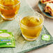 A glass cup of Twinings green tea with a tea bag in it on a marbled surface.