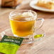 A glass cup of green tea on a saucer with a Bigelow green tea bag.