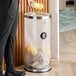 A clear acrylic round trash can with a stainless steel top and a 17-gallon capacity.