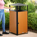 A square outdoor trash can with a covered top, made of steel and wood composite slats.