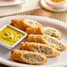 A plate of Crunch Factory Steak and Cheese Crunch Rolls with a bowl of yellow sauce.