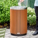 A round outdoor trash can with a wood composite slat design and a stainless steel open lid.