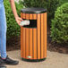 A round outdoor trash can with a wood composite exterior and a side opening.