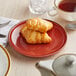 An Acopa Sedona Orange porcelain plate holding a croissant on a table with a cup of tea.
