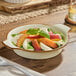 A round, shallow vanilla bean porcelain casserole dish filled with a fresh salad, placed on a wooden table.