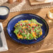 A blue porcelain coupe plate holding a fresh salad with greens, mandarin oranges, pecans, and pomegranate seeds.