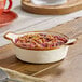 A small vanilla bean porcelain mini casserole dish with handles, filled with a berry crumble dessert.