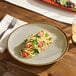 An Acopa Keystone porcelain plate with pasta, tomatoes, and basil on a wooden table.