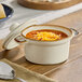 An 8 oz. vanilla bean porcelain mini casserole dish with a lid, filled with soup and topped with shredded cheese.